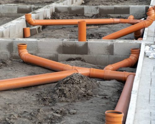 istockphoto-1361975446-612×612 New Installed pipework system. Sewer Line developed and mounted on the construction site. New Orange PVC plastic Drainage pipe Tube